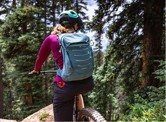 Mountainbiker med en Osprey-ryggsäck som cyklar genom en skogsstig.