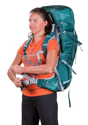 Eine Frau in einem orangefarbenen T-Shirt und einem blaugrünen Rucksack über den Schultern zieht den Nylon-Verstellgurt des Hüftgurts fest.