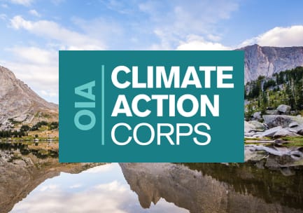 Das blaugrüne und weiße Logo des OIA Climate Action Corps über dem Foto einer bewaldeten Berglandschaft mit einem glasklaren, spiegelnden Bergsee und einem blauen Himmel.