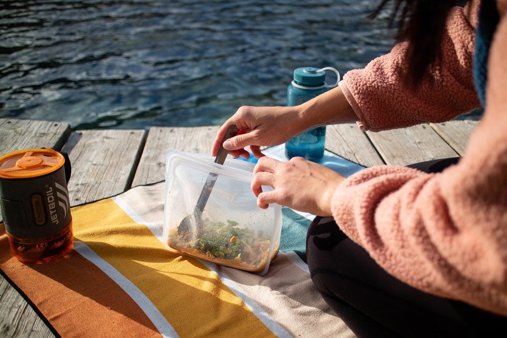A women mixing ingredients in a clear stasher bag on a dock surround by water