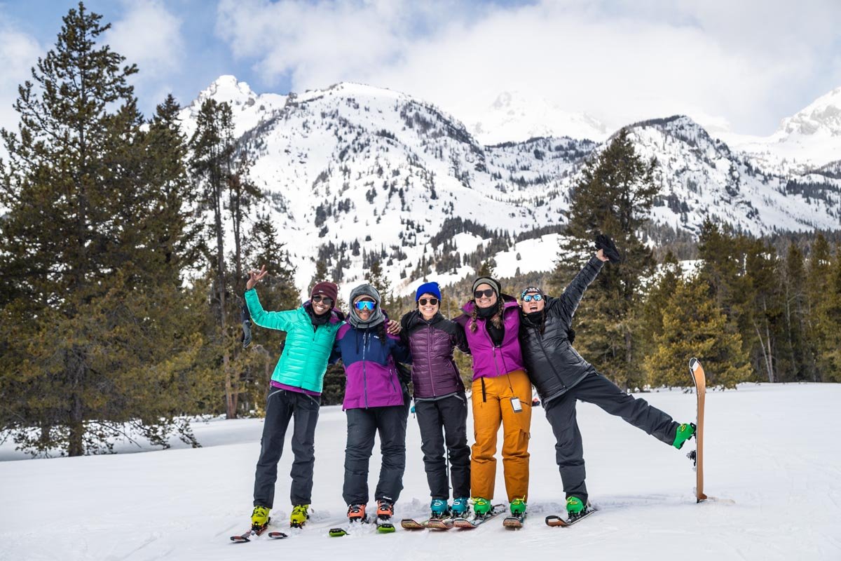 Five BIWOC women wearing skis on a mountain hugging and posing for a picture