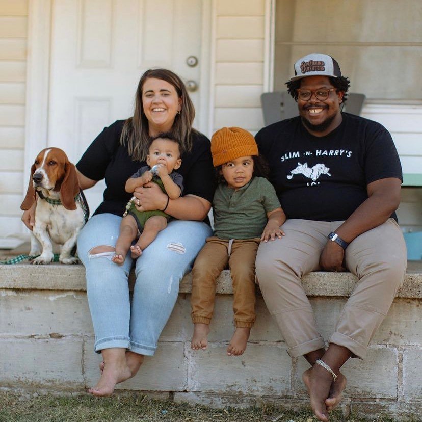 A man and woman holding their two kids and posing with their basset hound