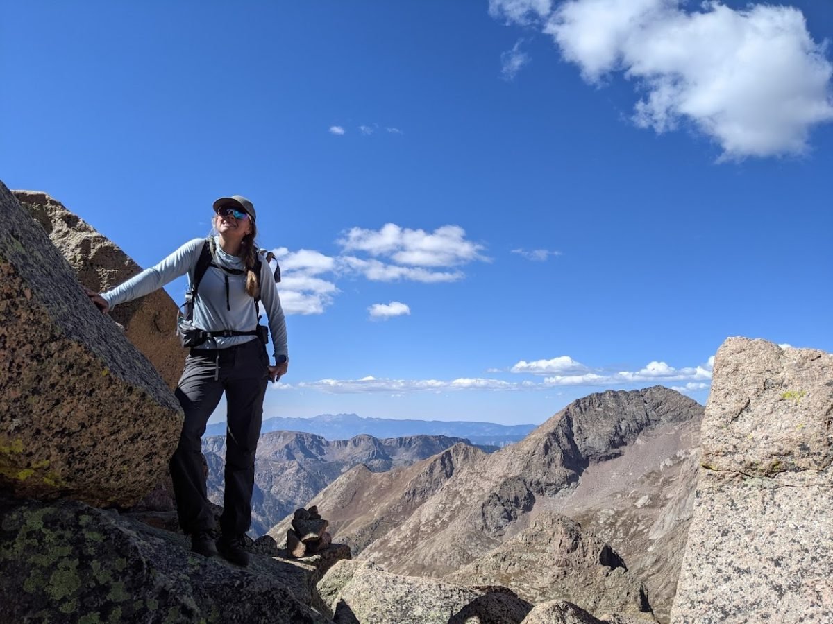 A woman posing next to a boulder atop a mountain