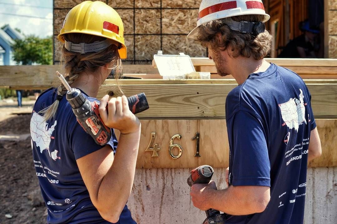 Two people wearing hard hats on a construction site, holding electric drills