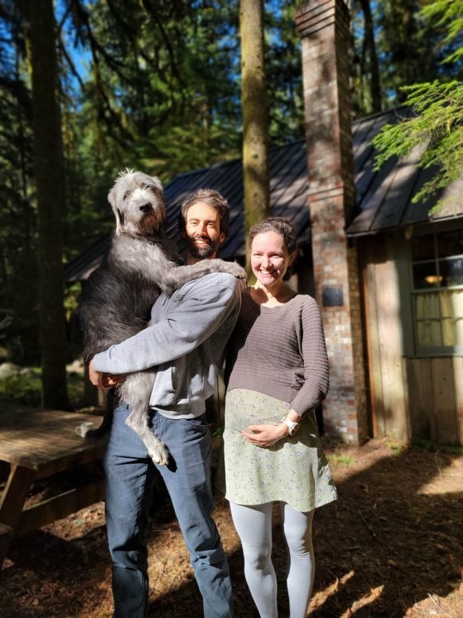 A man holding a dog, standing next to a woman with her hand on her belly, announcing a pregnancy