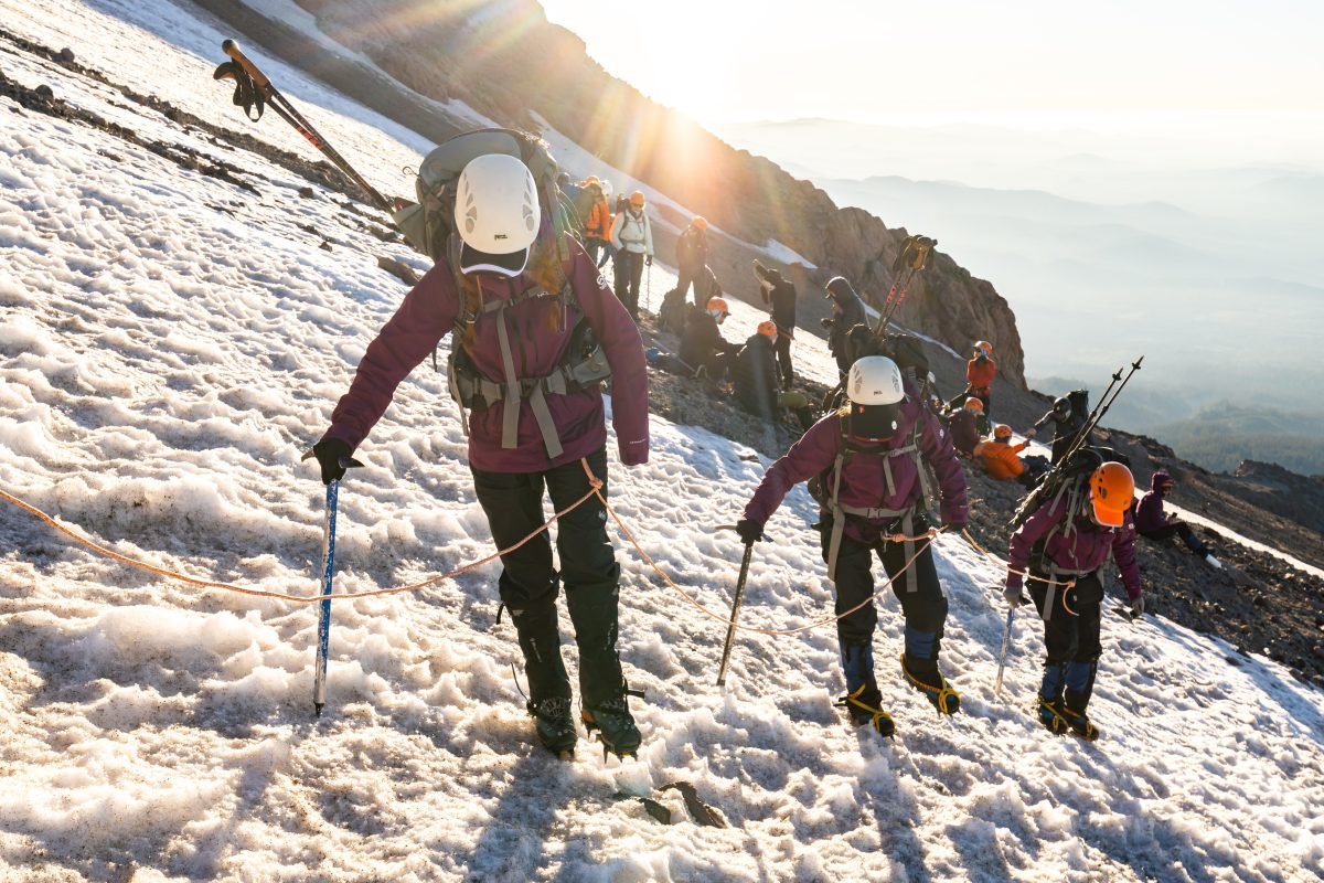 A group of climbers trekking up a snowy mountainside, all clipped together to a rope.