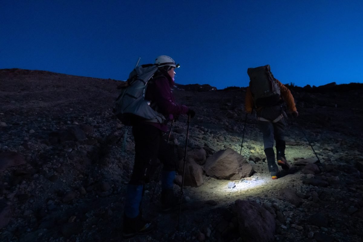 Two climbers walking on trail in the dark with headlamps lighting the way