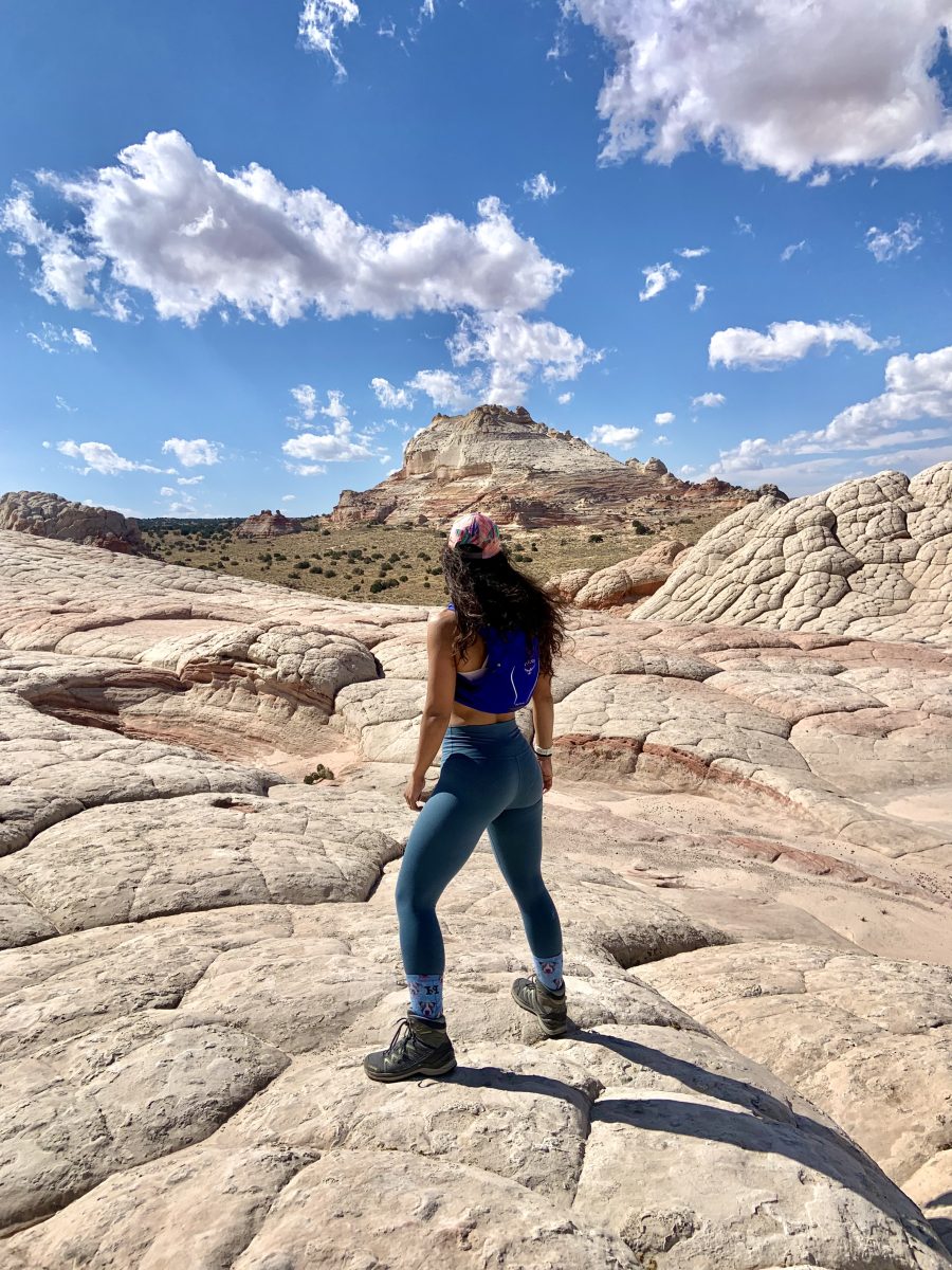 A woman standing on slick rock wearing a running hydration pack and looking into the distance