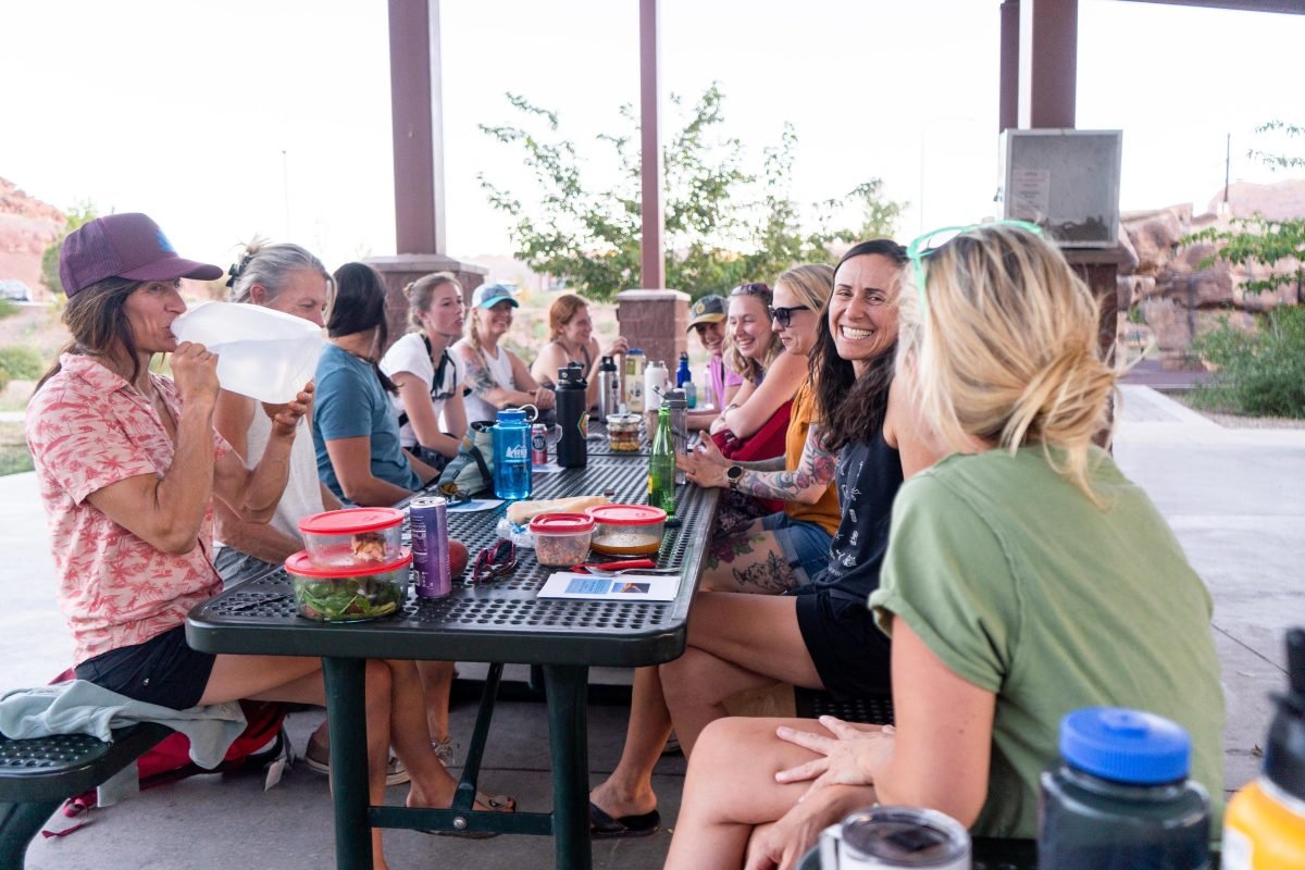 A group of women sitting around two park picnic tables chatting amongst each other