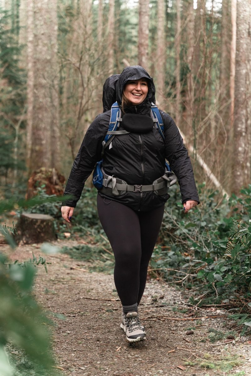 A woman in rain gear walking along the trail in her backpacking gear