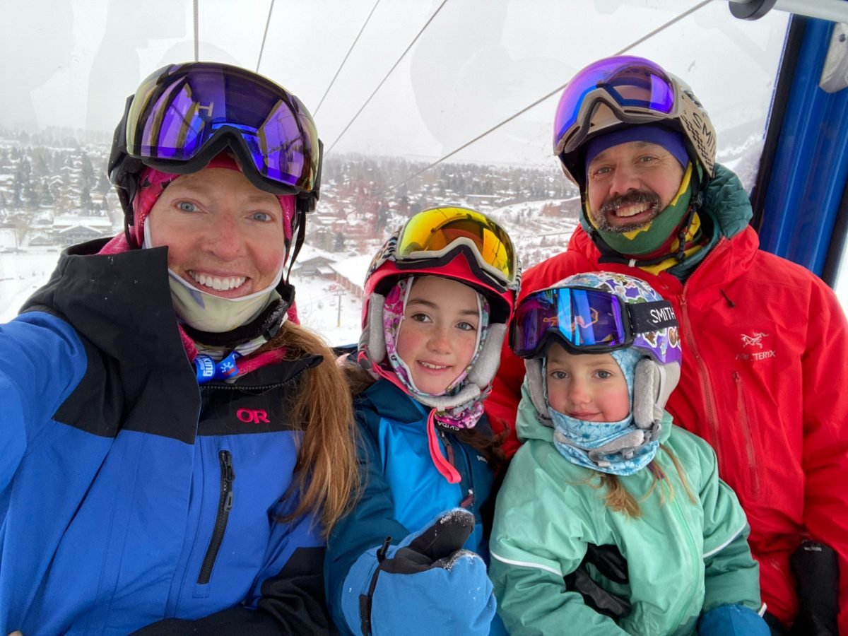 A man and woman in a gondola with their two kids, all wearing ski gear