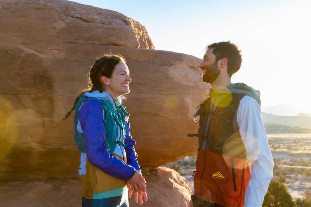Two people in running gear standing on a rocky trail, with a large boulder in the background