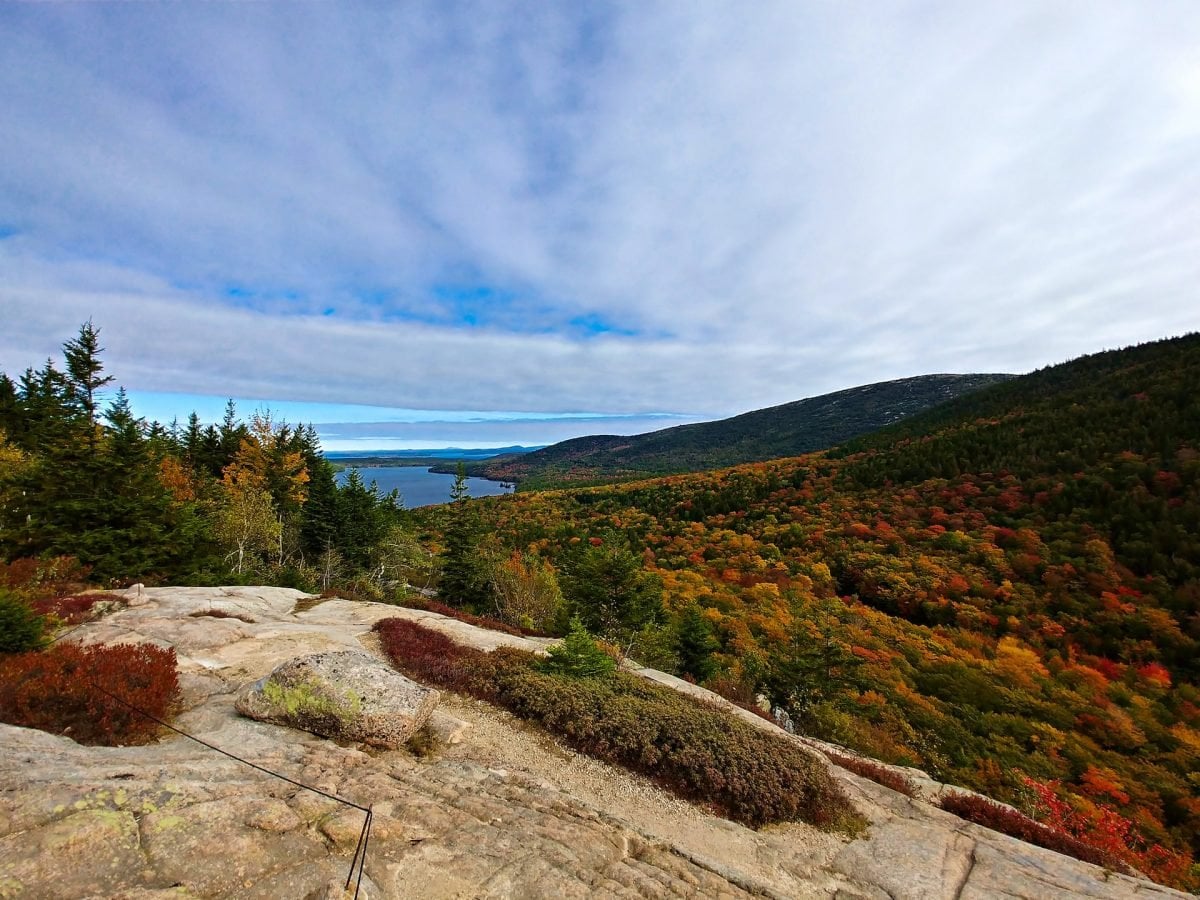 A landscape view of colorful trees and a body of water in the background from a rock overlook