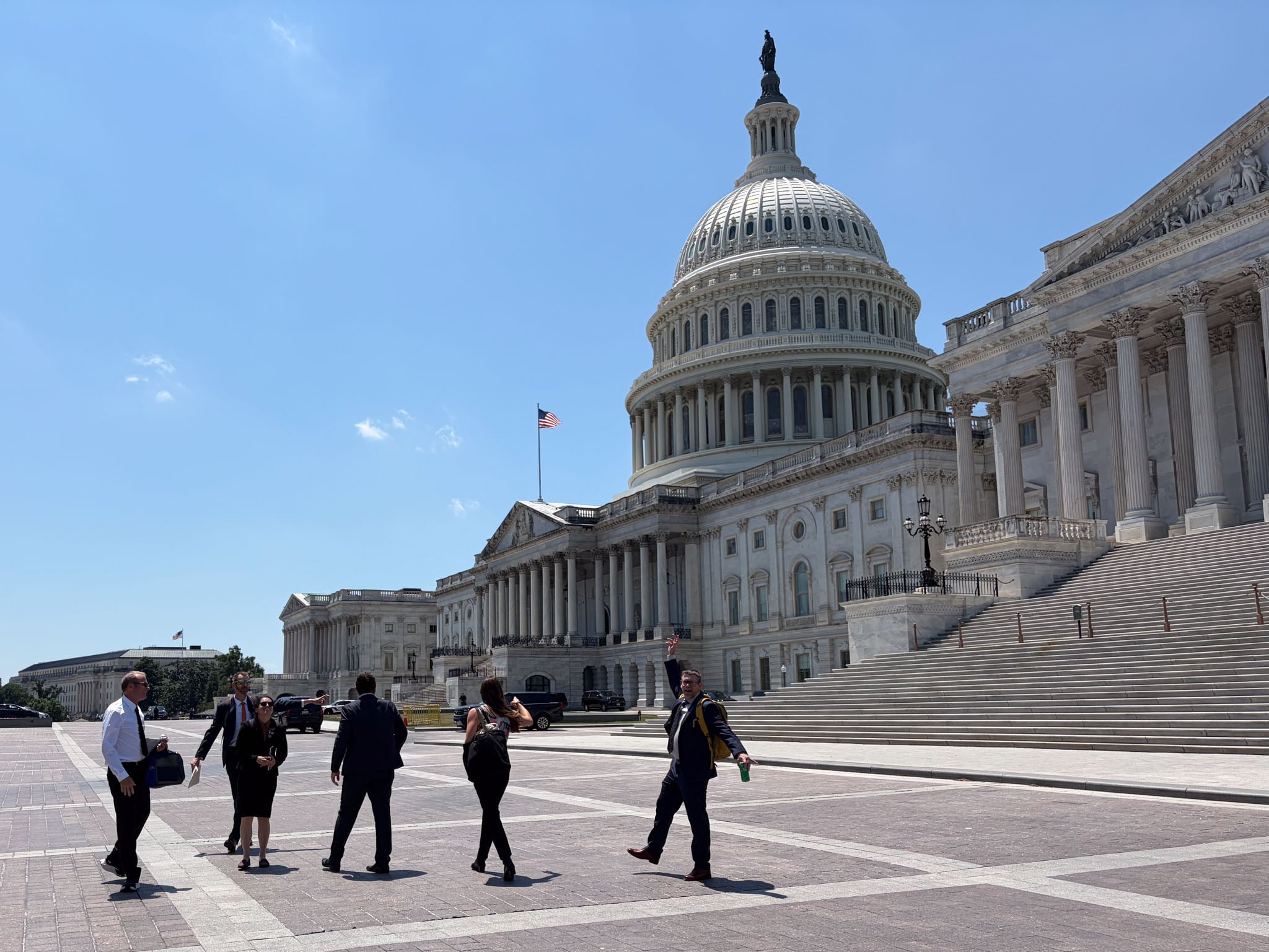 a group of people walk in front of the US Capitol building.