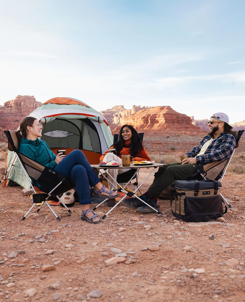 Three people lounge at a scenic desert campsite outfitted with an assortment of Campcore products.