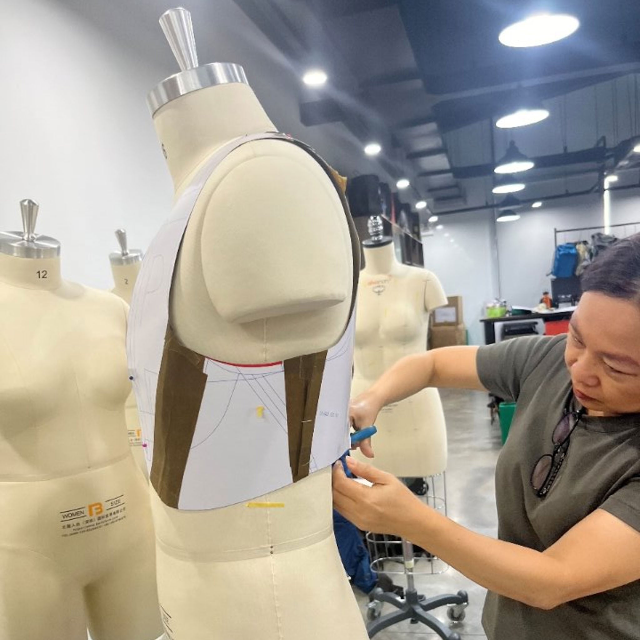 A person cuts a paper pattern on a mannequin. 