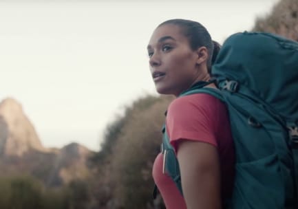 Color photo of a blond woman wearing a purple jacket and navy blue and gray Osprey pack against a blue sky. An orange sleeping pad and narrow yellow bag are strapped to the exterior at the bottom
of the pack. The photo is signed in black marker and says, &ldquo;A great pack &mdash; &ldquo;100 miles&rdquo; Wind Rivers, Big Sandy to Green River. Fran Schmuch Aug 1992&rdquo;