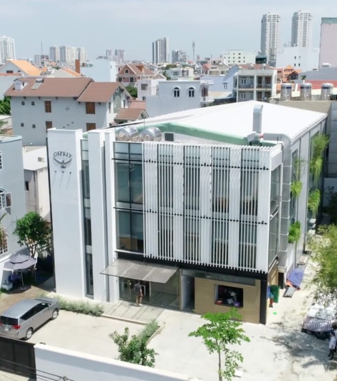 Modern office building amid a dense urban landscape, with vertical white, stainless steel and glass panels. A stainless steel Osprey logo is on the main fa&ccedil;ade on the left. Green plants are growing in planters on the side of the building.