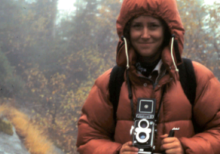 A woman poses in nature with a vintage camera.